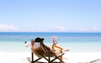 person relaxing in a beach chair reading a book facing the ocean