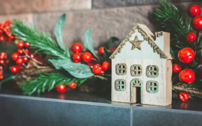 a small wooden house on a mantle near holly berries