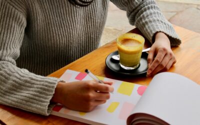 person's arms on wooden table with planner and espresso