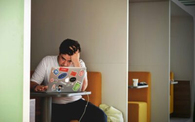 man looking at a sticker-covered laptop from a cube looking nervous